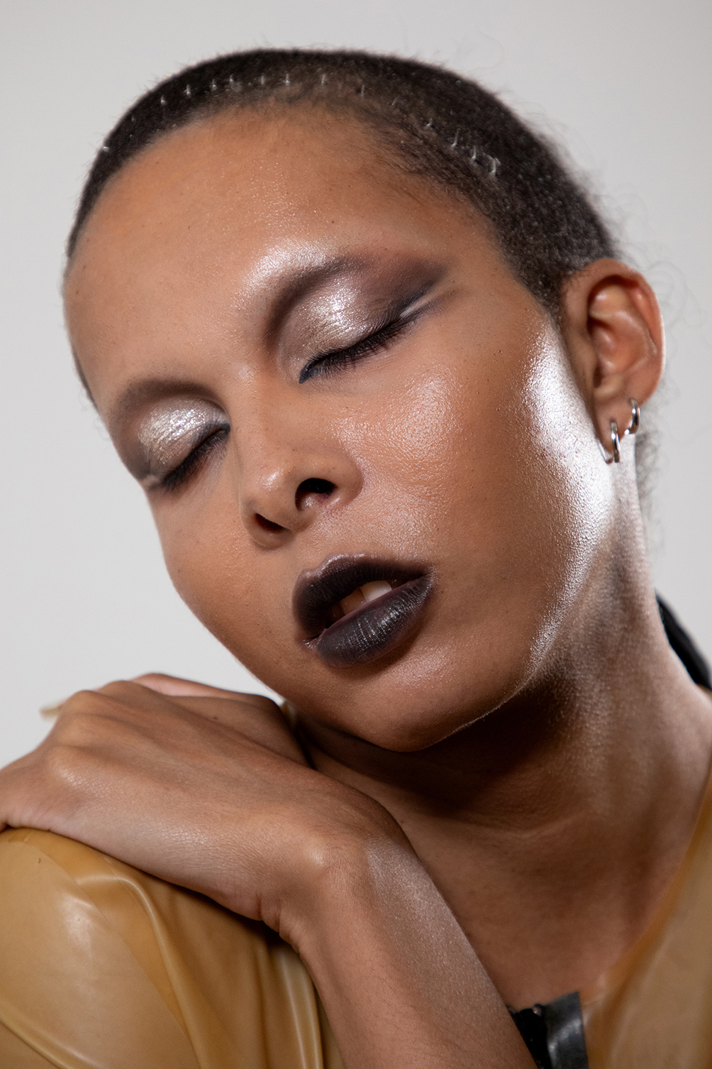 Valeria with dramatic eye makeup posed with her head resting on her shoulder against a gray background